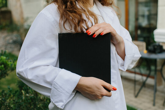 Magazine or book image mockup. Young attractive girl holding a closed book in her hands while standing in the yard.