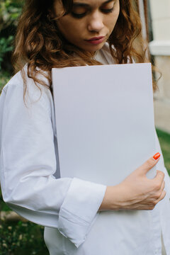 Magazine or book image mockup. Young attractive girl holding a closed book in her hands while standing in the yard.