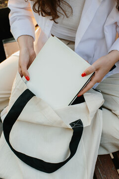 Magazine or book image mockup. A young hipster girl at a table in a coffee shop takes out a magazine from a canvas shopper bag.