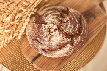 Freshly baked rye bread on a yeast-free starter and on a mixture of whole grain, rye and wheat flour. It lies on a napkin, next to a dried flower with grains. Selective focus. High quality photo