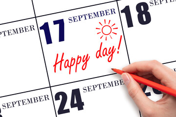 Hand writing the text HAPPY DAY and drawing the sun on the calendar date September 17