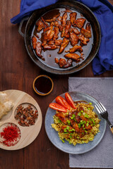 Fried chicken pieces in soy and pad thai sauce in a pan on a blue napkin on a table with a plate and spices.