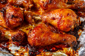 Chicken legs baked in sauce and spices with a crispy crust on foil close-up.