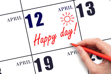 Hand writing the text HAPPY DAY and drawing the sun on the calendar date April 12