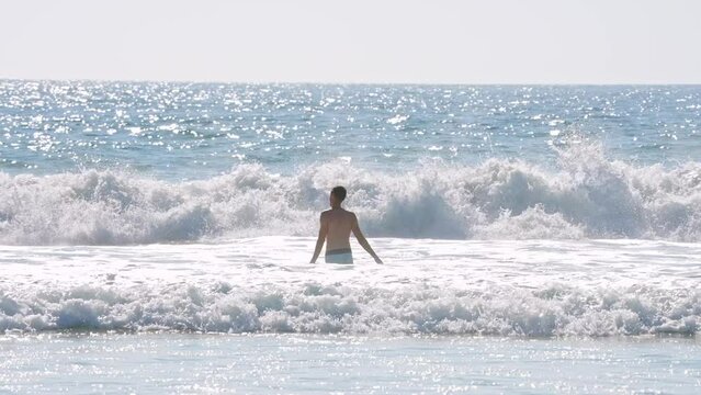 Rear view of carefree shirtless man swimming and splashing in the waves in the Pacific Ocean in San Diego on a sunny day.