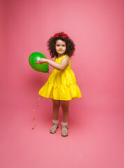 Happy birthday celebration with flying balloons of a charming cute little girl in a yellow dress isolated on a pink background.