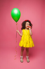 Fototapeta na wymiar Happy birthday celebration with flying balloons of a charming cute little girl in a yellow dress isolated on a pink background.
