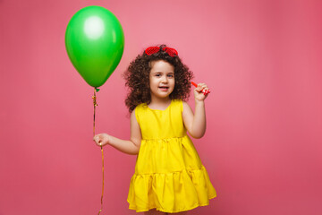 Obraz na płótnie Canvas Happy birthday celebration with flying balloons of a charming cute little girl in a yellow dress isolated on a pink background.