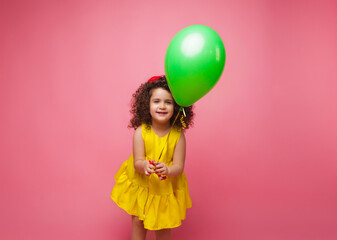 Fototapeta na wymiar Happy birthday celebration with flying balloons of a charming cute little girl in a yellow dress isolated on a pink background.