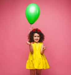 Happy birthday celebration with flying balloons of a charming cute little girl in a yellow dress isolated on a pink background.