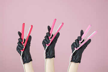 Three hands in black rubber gloves hold pink hair curlers on a pink background. Space for text .Banner