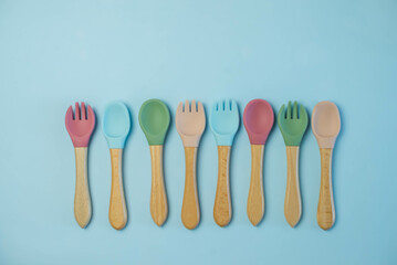 A set of colored silicone forks and spoons with a wooden handle. Baby feeding and nutrition concept. Top view, flat lay.