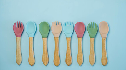 A set of colored silicone forks and spoons with a wooden handle. Baby feeding and nutrition concept. Top view, flat lay.