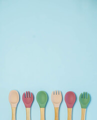 A set of colored silicone forks and spoons with a wooden handle. Baby feeding and nutrition concept. Top view, flat lay.
