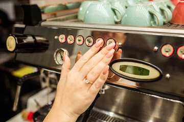 Hands of female barista pressing button on machine while making fresh coffee.