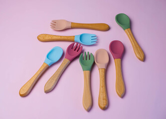 A set of colored silicone forks and spoons with a wooden handle. Baby feeding and nutrition concept. Top view, flat lay.