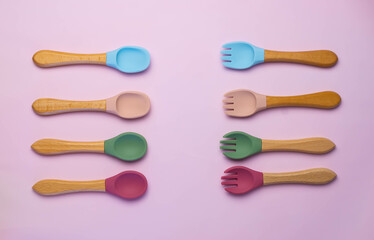 A set of colored silicone forks and spoons with a wooden handle. Baby feeding and nutrition concept. Top view, flat lay.