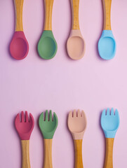 A set of colored silicone forks and spoons with a wooden handle. Baby feeding and nutrition concept. Top view, flat lay.