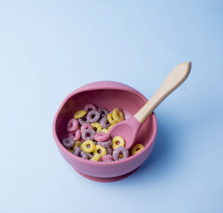 Children's silicone bowl with corn flakes. Baby feeding and nutrition concept. Top view, flat lay.