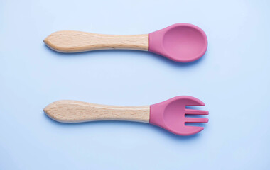 A set of colored silicone forks and spoons with a wooden handle. Baby feeding and nutrition concept. Top view, flat lay.