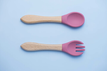 A set of colored silicone forks and spoons with a wooden handle. Baby feeding and nutrition concept. Top view, flat lay.