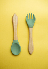 A set of colored silicone forks and spoons with a wooden handle. Baby feeding and nutrition concept. Top view, flat lay.