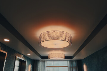 A glowing and lit drum light with black metal accents on a warm ceiling