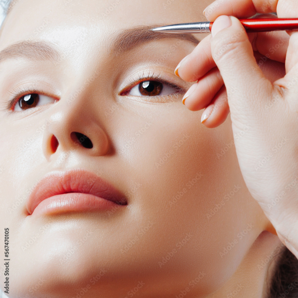 Wall mural Makeup artist working with brush on eyebrows of young beautiful woman