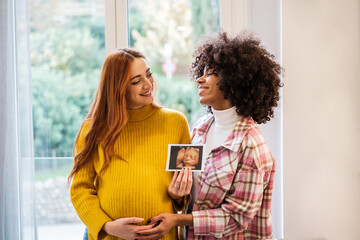 Couple of women presenting the pregnancy photo proud of their future. Concept: maternity, pride, integration