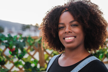 Close-up portrait of young woman with curly hair and African American features smiling outdoors. Concept: lifestyle, curly hair