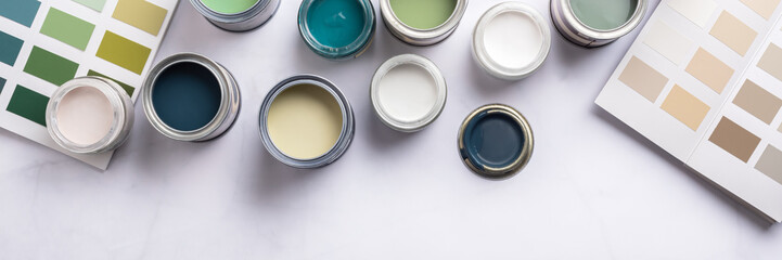 Tiny sample paint cans during house renovation, process of choosing paint for the walls, different green, blue and beige colors, color charts on background, banner size
