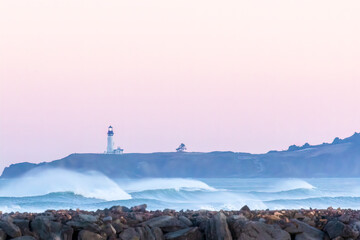 Yaquina Head Lighthouse in pastel sunrise with spindrift on waves