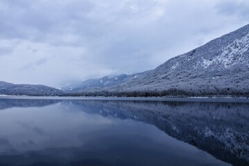 View of lake Bohinj with forest covered mountains slopes rising above in Julian alps, Gorenjska, Slovenia in winter