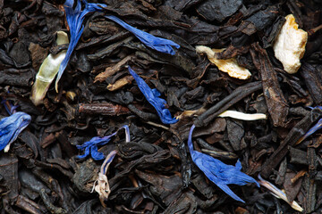 Closeup of black tea with orange, lemon peels and cornflower petals background