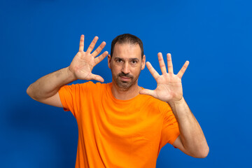 Front view of a Caucasian man with short hair wearing an orange t-shirt with his palms facing him, camera facing palm, touching an interactive virtual screen.