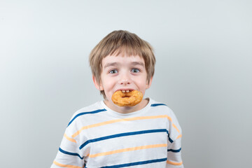 A blond-haired, blue-eyed boy holds a doughnut in his teeth.
