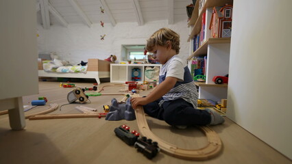Child playing in bedroom alone. One small boy plays at home with wooden tracks. Childhood development