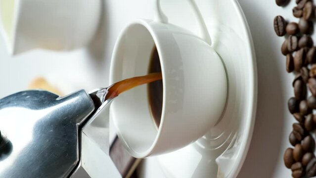 The process of pouring coffee from a geyser moka coffee maker into a white cup