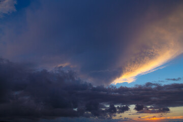 Stormy setting sun with warm light illuminates a dark blue clear sky with such a white cloud.