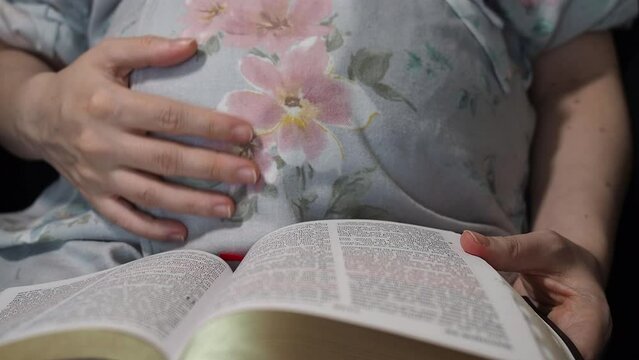 Pregnant caucasian woman caressing her belly and reading the holy bible