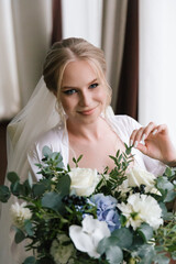 Morning preparations of a beautiful, sexy bride with a wedding bouquet in lingerie, a bathrobe in a hotel, where she puts on shoes in a wedding dress