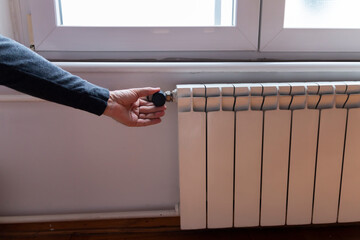 Cropped view of man's hand adjusting thermostat on white heating radiator. Consumption of natural...
