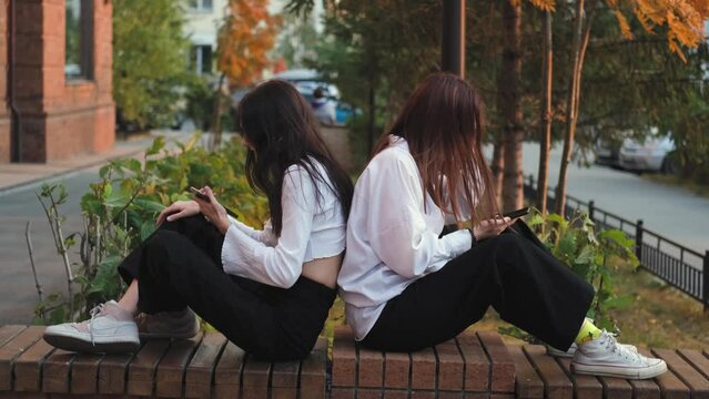 Two girlfriends are arguing, sitting on a street bench apart, young women are in conflict. Teenage friendship issues