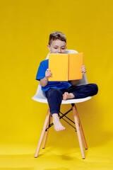 Little cheerful blond green-eyed boy 5-6 years old in a stylish blue T-shirt holding book and...