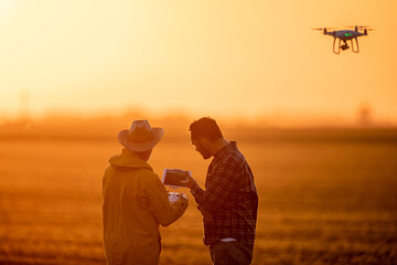 Silhouettes of farmers driving drone at sunset
