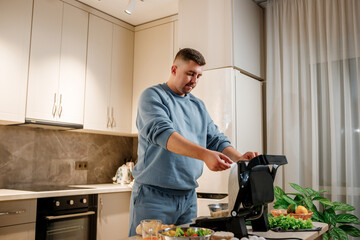 Man prepares delicious juicy meat steak on an electric grill on wooden table. Smoke in the home kitchen