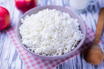 dairy product cottage cheese in a plate with a glass of milk and apples on a wooden background
