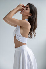 Young woman with hairstyle and makeup in sensual white dress posing in studio, lookig at the side, isolated grey background.