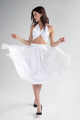 Naklejka premium Full length image of young woman with hairstyle and makeup in white dress posing in studio, it spins, isolated grey background.