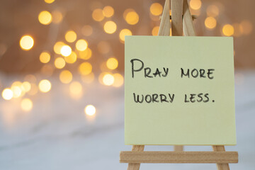 Pray more, worry less, handwritten message on note with blurred bokeh background. A closeup....